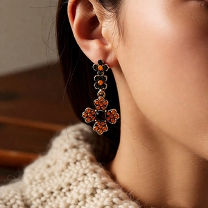 Close-up of vintage gold earrings with orange and black zircons on model ear