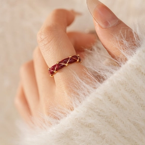 Macro shot of deep red enamel ring with golden crisscross patterns worn on finger