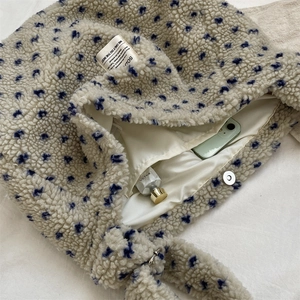 Detail view of plush beige tote with blue patterns featuring a silver magnetic snap closure