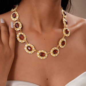 Detail of vintage gold necklace with red gemstone and white floral enamel on model