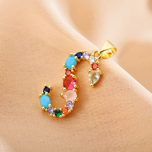 Macro detail of gold S-letter pendant with multi-colored crystals on soft fabric