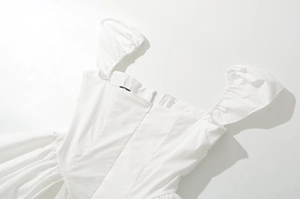 Close-up of white V-neck pleated dress featuring bubble sleeves and back zipper