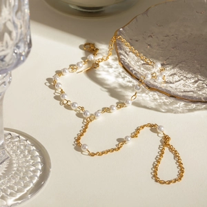 Detail of 18k gold chain and white pearls on a glass plate under natural sunlight