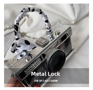Detail of silver camera-shaped handbag with hardware clasp and polka dot ribbon handle