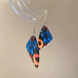 Macro shot of colorful acrylic butterfly wing earrings with vibrant blue and orange patterns