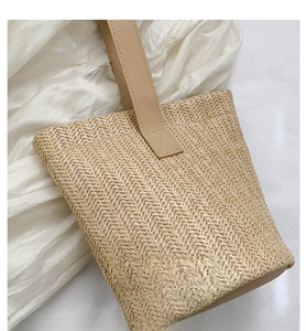 Close-up of natural woven straw bucket bag texture with beige leather handle and herringbone pattern