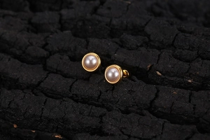 Close-up of minimalist gold-rimmed pearl studs on a dark textured wood background