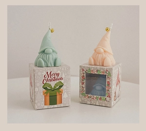 Detailed view of mint green and pink gnome candles with gold bells in Christmas gift boxes