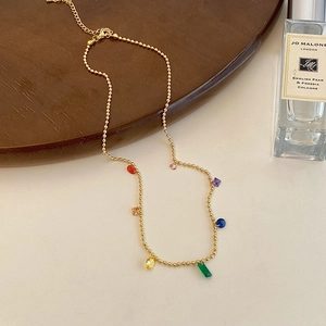 Detailed close-up of golden bead chain necklace with colorful gemstone pendants on wood