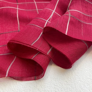 Elegant thin red striped silk wool scarf draped on textured beige surface