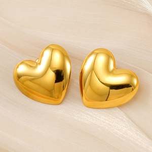 Macro view of 18K gold heart-shaped earrings on textured cream fabric background