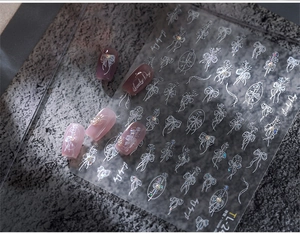 Macro detail of white embossed 3D heart and bow nail stickers on purple matte nails