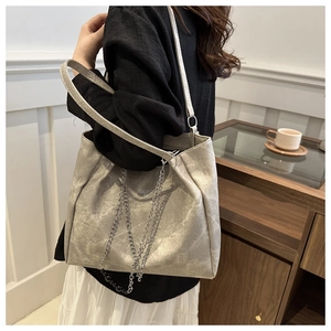 Detail of silver leather tote bag featuring a metallic chain and decorative black bead charm
