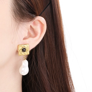 Detail of square gold embossed eye stud earrings featuring hanging baroque pearl drops