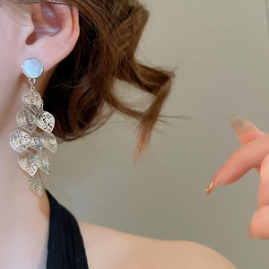 Close-up of silver leaf tassel earrings with white opal stud worn by a model