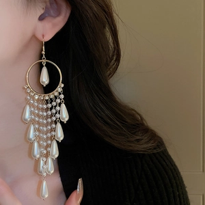 Close-up of golden geometric earrings with long white pearl tassels worn by a model