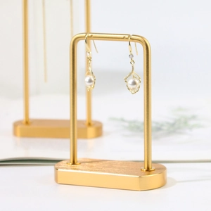 Elegant gold pearl drop earrings showcased on a minimalist metal display stand
