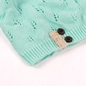 Detail of mint green knitted beanie showing leaf openwork pattern and lace button