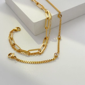 Macro shot of gold double-layer chain bracelet featuring clear zircon stones on a white stand