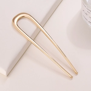 Detail of a minimalist gold-toned U-shaped metal hair pin on a white textured surface