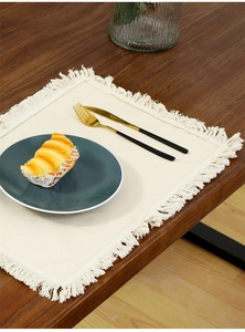 Macro detail of cream linen placemat with fringe on a dark wood dining table