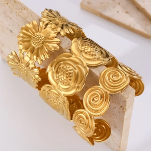 Detailed view of three gold-plated open bangles featuring floral and swirl relief patterns