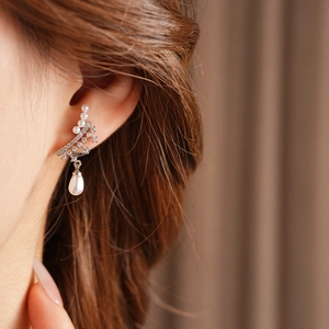 Detailed view of silver needle drop earring with zircon and pearls on model's ear