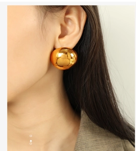 Macro detail of a model wearing a minimalist large polished gold spherical stud earring