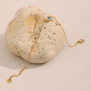 Detail of 18K gold plated stainless steel evil eye bracelet on a beige stone display