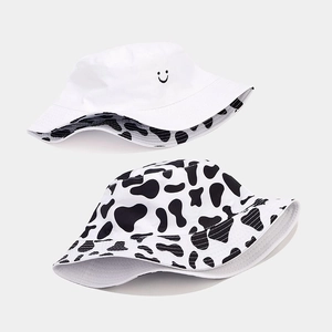 Detail of reversible bucket hat showing cow print side and white side with smiley embroidery