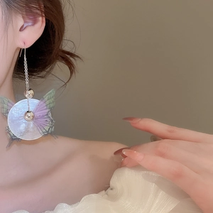 Primo piano di una modella con lunghi orecchini a farfalla con nappe e ciondoli in conchiglia