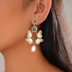 Detail of golden butterfly earring with green gems and hanging pearl on model