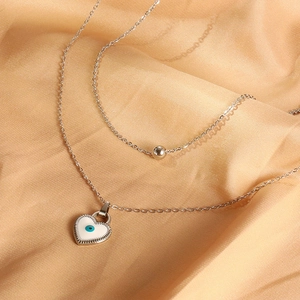 Macro detail of silver layered heart evil eye necklace on champagne satin fabric