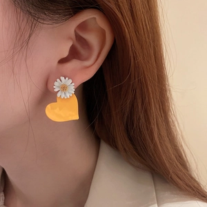 Close-up of asymmetric daisy and heart drop earring worn by a female model