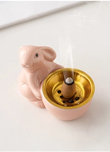 Close-up of a pink ceramic rabbit incense burner holding a golden bowl with an incense cone