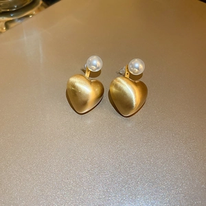 Macro shot of gold heart earrings with matte brushed texture and white pearl accents