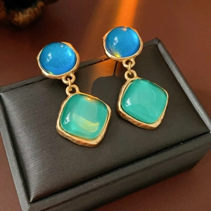 Détail de boucles d'oreilles vintage dorées avec pierres bleue et verte sur écrin