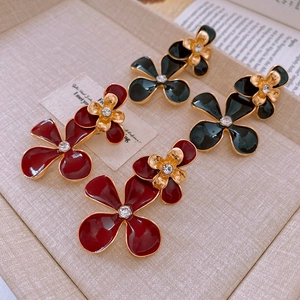Detail of red and black enamel flower earrings with crystal center on a beige tray