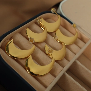 Three pairs of golden moon-shaped minimalist stud earrings in a jewelry storage box