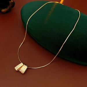 Detail of gold snake chain necklace with rectangular textured pendant and clear crystals