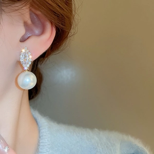 Close-up of elegant gold earrings with geometric zircon and large white pearls on a model
