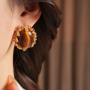 Close-up of vintage gold-plated earrings with large brown tiger eye stones on a model