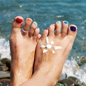 Detailed view of silver toe ring on foot at beach with ocean waves and sun-shaped lotion