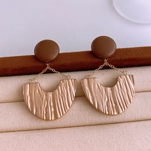 Macro view of gold U-shaped pleated earrings with brown resin studs on a jewelry display
