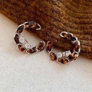 Gros plan des boucles d'oreilles en C tissées avec ruban léopard et zircons