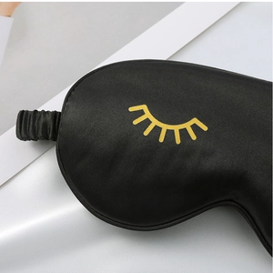Detail view of the black silk sleep mask featuring a cute yellow eyelash print, soft and smooth.
