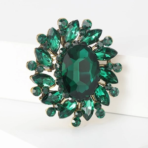 Macro shot of an ornate bronze brooch with a large emerald green crystal and teardrop accents