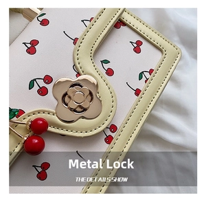 Close-up of golden flower clasp and cherry print on a stylish cream shoulder bag