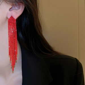 Close-up of red tassel earrings with sparkling rhinestones worn by a model