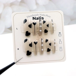 Détail de faux ongles faits main avec motifs de cœurs noirs et accents de perles